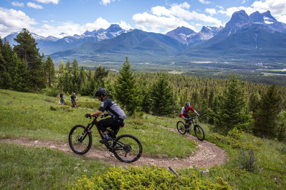 A group of people on mountain bikes going up a hill at the Canmore Nordic Centre.