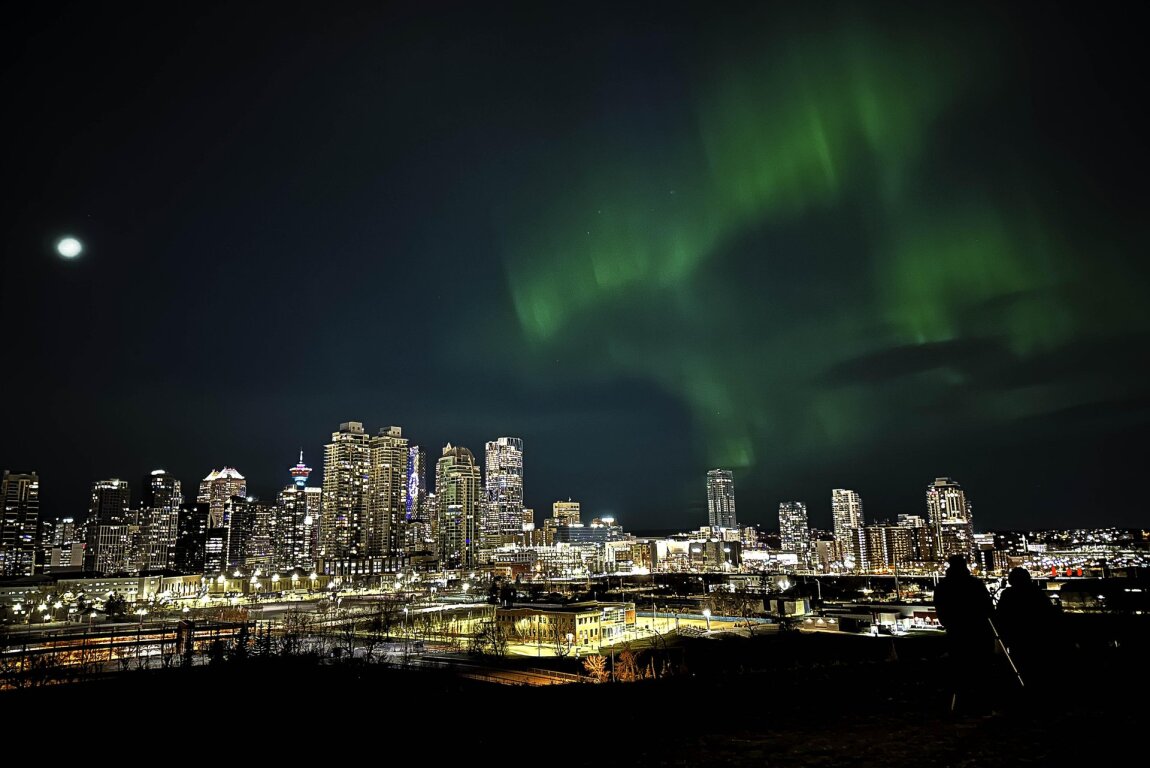 Northern Lights glowing above the Calgary skyline, featuring downtown buildings at night.