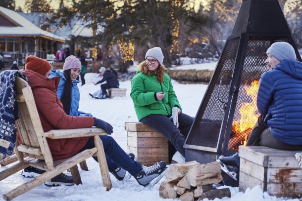 group of friends warms up by a wood fire pit on Bowness Lagoon after skating
