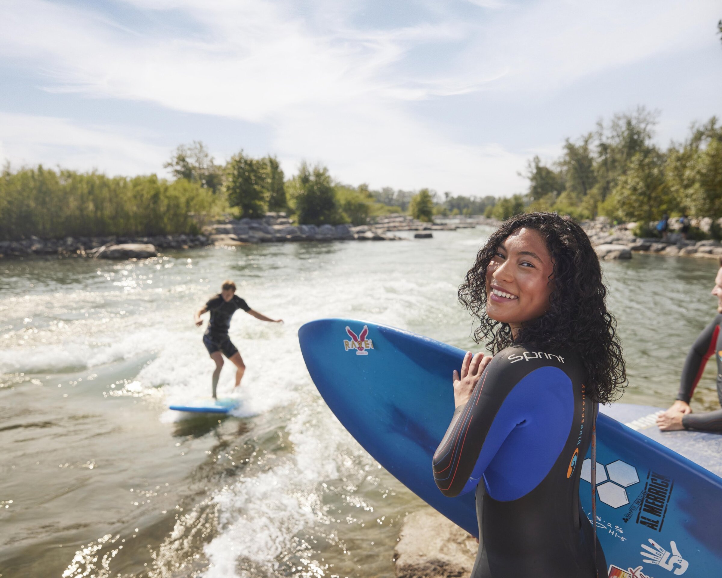 Girl holding her surfboard smiling on the bank of bow river