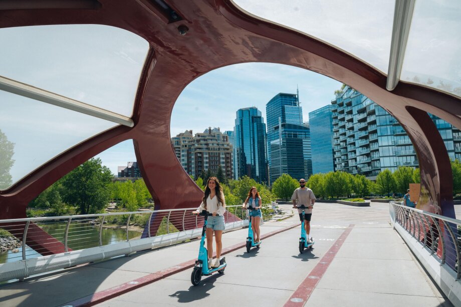 Three people ride e-scooters along the Peace Bridge.
