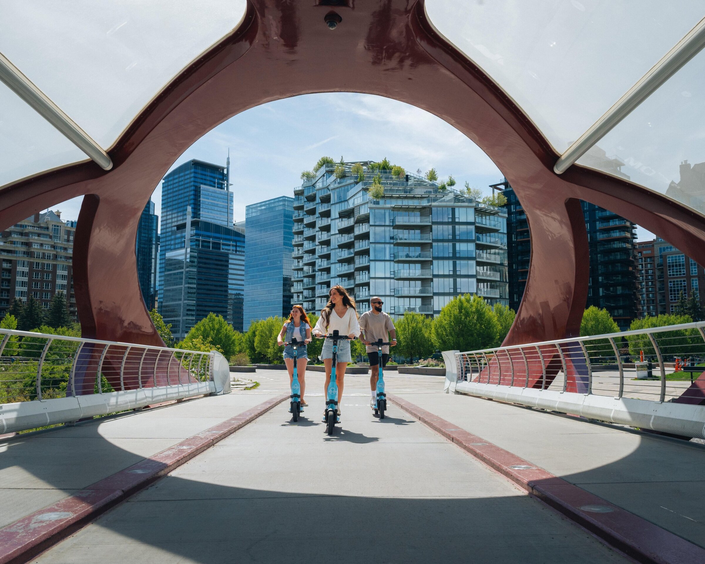 3 friends on e-scooters on the peace bridge in Calgary
