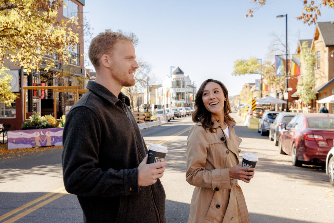 A man and a woman cross Kensington Road holding coffee cups.