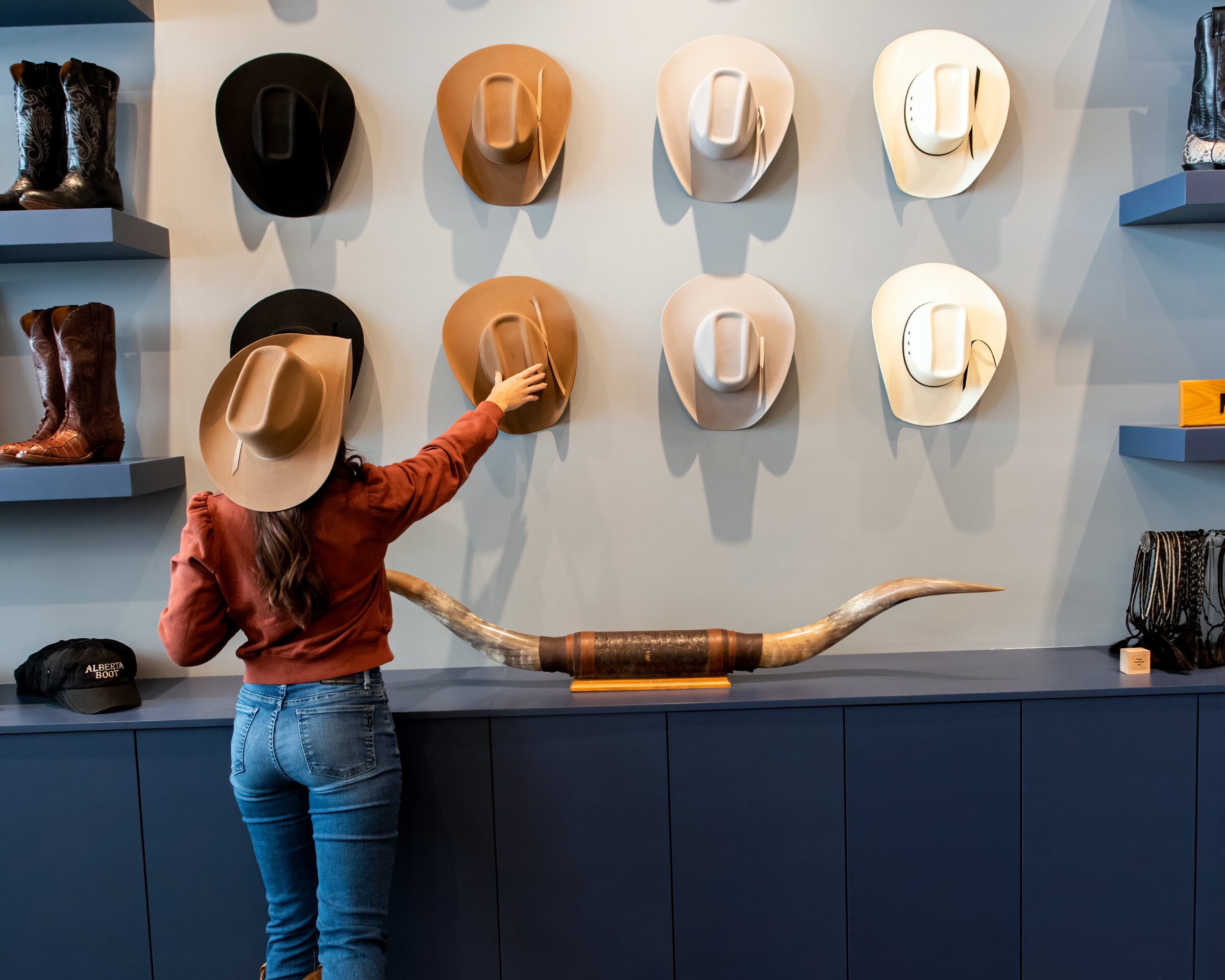 Woman grabbing a cowboy hat off of a wall of hats